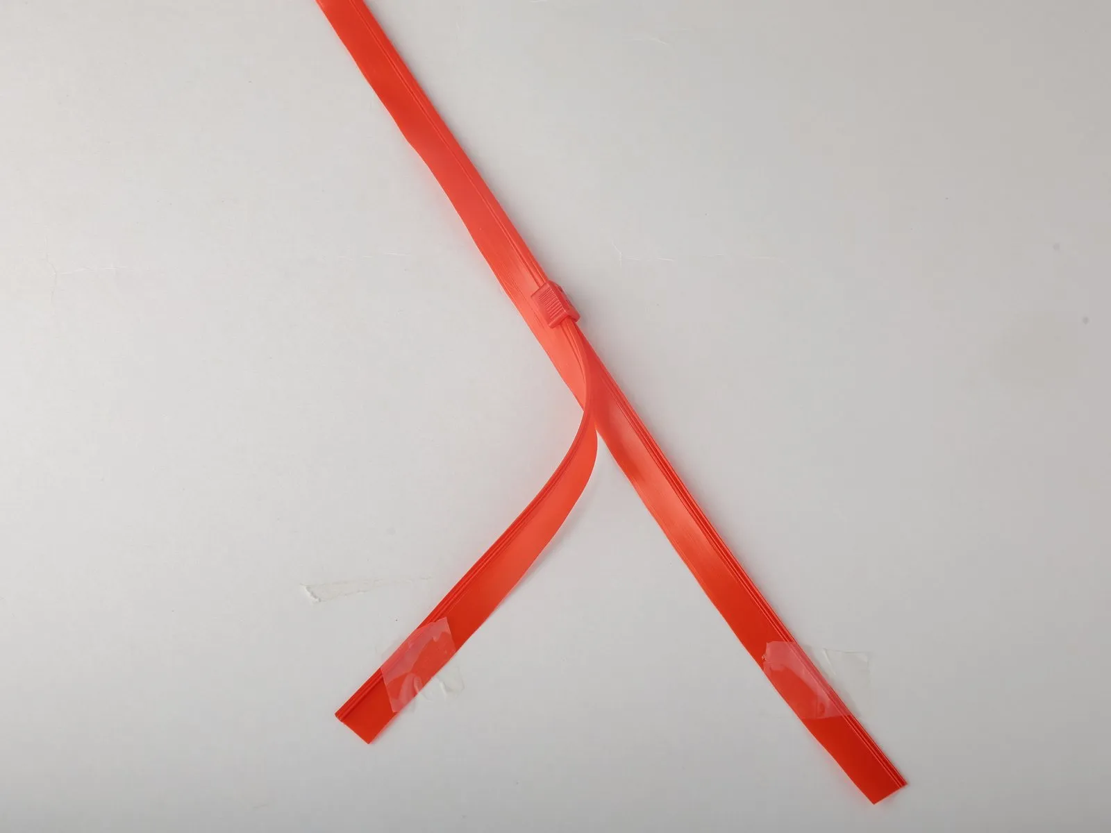 Client photo of a red plastic zipper strip folded into a V on a grey ground, held down with clear tape