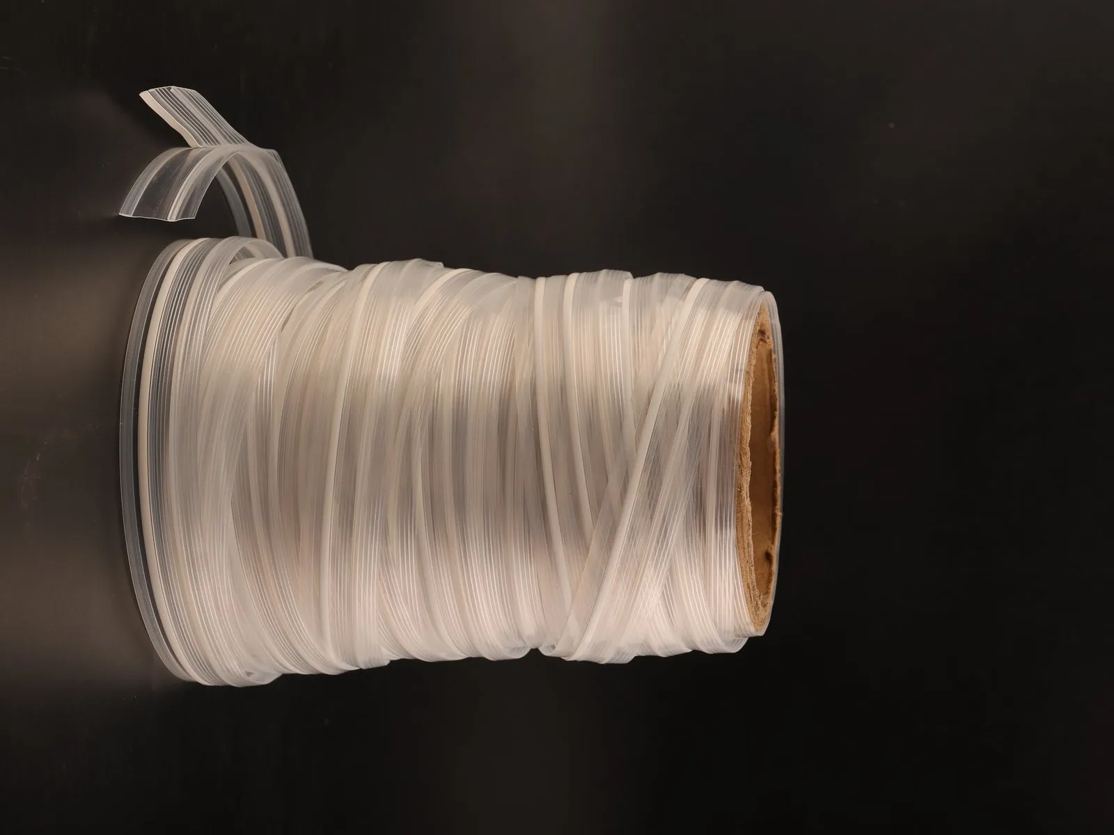 Client photo of a reel of clear plastic zipper profile on a cardboard core against a black backdrop