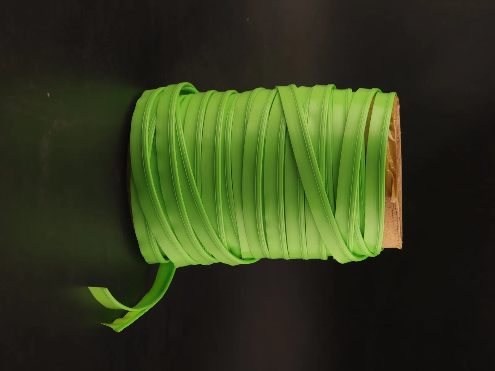 Client photo of a reel of green plastic zipper tape on a cardboard core against a black backdrop